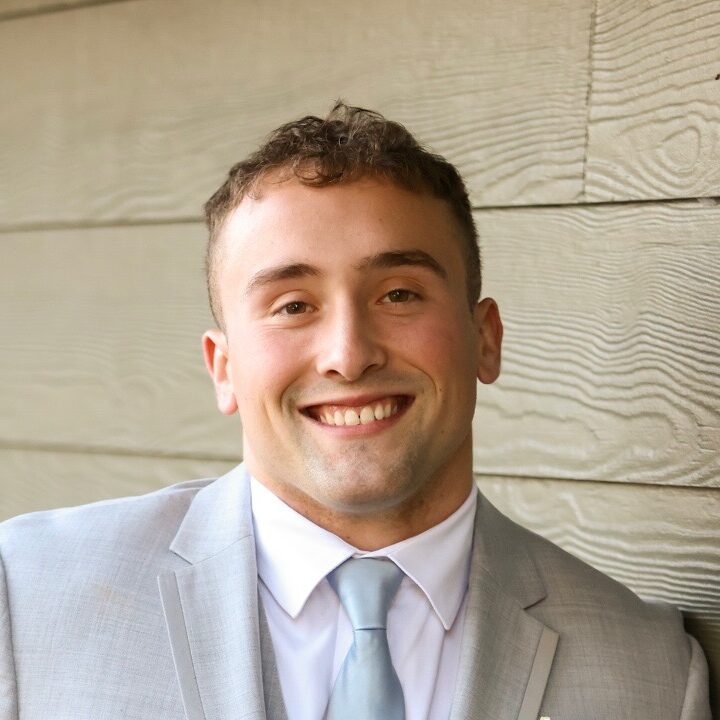 Seth in a suit and tie smiling in front of a blank wall